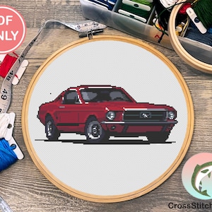 Könnte beinhalten: Ein Kreuzstichmuster eines klassischen roten Mustang-Autos, das in einem hölzernen Stickrahmen dargestellt wird. Das Bild enthält Garnrollen, ein Maßband und einen "PDF ONLY"-Aufkleber. Das Design befindet sich auf weißem Hintergrund.