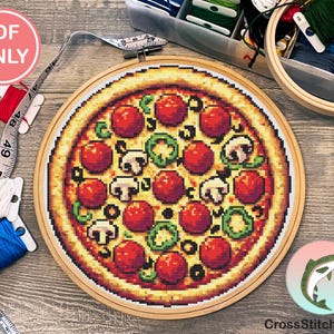 May include: A cross-stitch pattern of a pizza with pepperoni, mushrooms, and green peppers. The pizza is in a wooden embroidery hoop. The image includes the text "CrossStitchSalmon" and a salmon fish logo.