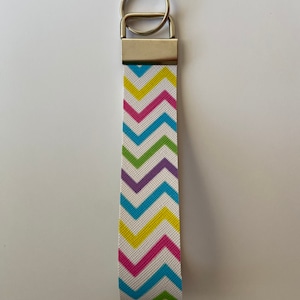 May include: A colorful chevron patterned key chain with a silver key ring. The pattern features pink, yellow, green, and blue chevron stripes on a white background.