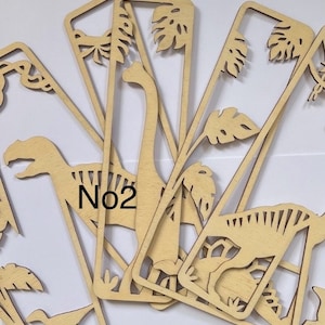 May include: A set of six wooden bookmarks featuring dinosaur silhouettes and tropical leaves. The bookmarks are laser cut and have a natural wood finish. The number "No2" is visible on one of the bookmarks.