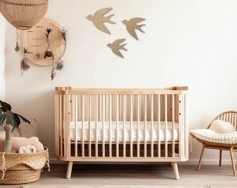 Puede incluir: Una cuna de madera con un colchón blanco y una alfombra blanca debajo. Hay tres recortes de pájaros de madera en la pared detrás de la cuna.