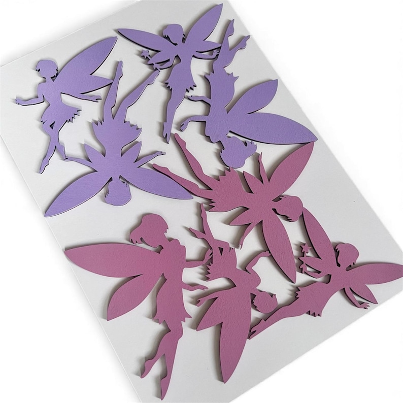 May include: A collection of fairy cutouts in shades of purple and pink. The fairies have detailed wings and are arranged on a white background. The cutouts are likely made of paper or cardstock and are suitable for crafts or decorations.