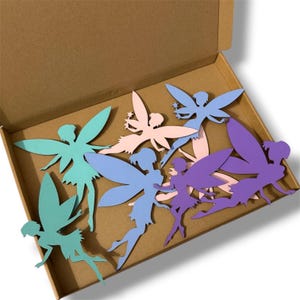 May include: A collection of colorful fairy cutouts in a cardboard box. The fairies are in shades of teal, light blue, pink, and purple. Each fairy has detailed wings and a silhouette design. The box is open, revealing the fairies inside.