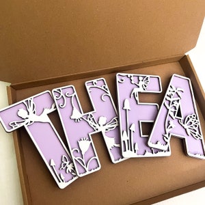 May include: Purple wooden letters spelling "THEA" with a fairy and floral design. The letters are in a box.