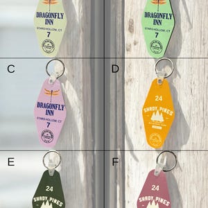 May include: A collection of vintage-style hotel keychains in various colors. The keychains feature the text "Dragonfly Inn" and "Shady Pines Retirement Home" with room numbers. Each keychain has a metal ring for attachment.