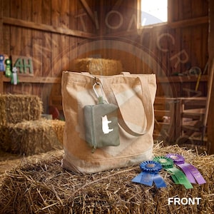 May include: A beige canvas tote bag with a small olive green zippered pouch attached by a silver carabiner. The pouch features a white silhouette of a dog. Three circular award ribbons in blue, green, and purple are placed in front of the bag.