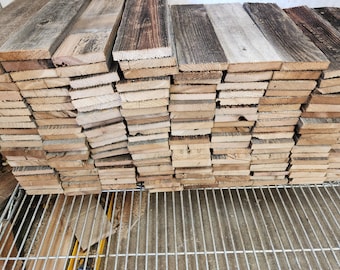 May include: A stack of reclaimed wood planks, varying in shades of brown and gray, with visible grain and texture. The planks are neatly arranged, suggesting a supply for woodworking or rustic decor projects.
