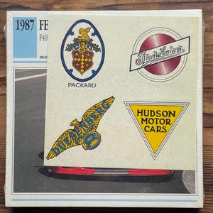 Op de afbeelding: Een pakket vintage auto-embleemstickers. De stickers tonen logo's voor Packard, Studebaker, Duesenberg en Hudson Motor Cars. Het pakket bevat ook de tekst "1987 FE F40 HIGH".