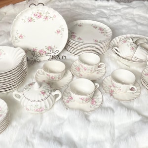 Può includere: Un servizio da tè in porcellana vintage completo con un motivo floreale a rose. Il set comprende piatti, ciotole, piattini, tazze da tè e una zuccheriera. I bordi dei piatti e delle ciotole hanno un bordo dorato.