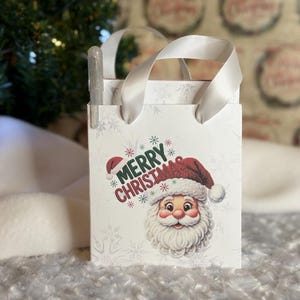 May include: A small white gift bag with a Santa Claus graphic and the words "Merry Christmas." The bag has white ribbon handles and a pen clipped to the side. The Santa graphic features a red hat and a white beard.
