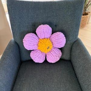 May include: A purple and yellow flower-shaped pillow on a dark gray armchair.