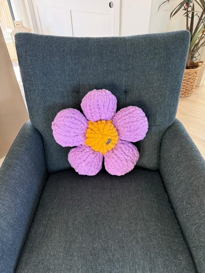 May include: A purple and yellow flower-shaped pillow on a dark gray armchair.