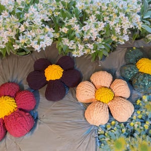 May include: Four crocheted flower-shaped cushions in different colours. The cushions are purple, pink, red, and green. Each cushion has a yellow centre.
