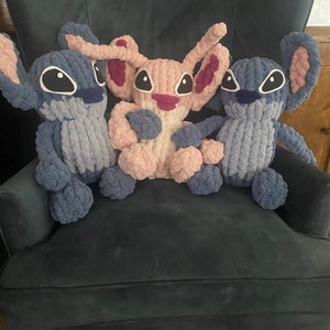 以下が含まれることがあります： 青いアームチェアに3つのぬいぐるみが置かれています。ぬいぐるみは糸でできており、映画リロ＆スティッチのスティッチの形をしています。1つのぬいぐるみはピンクで、他の2つは青です。