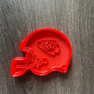 May include: Red plastic cookie cutter shaped like a football helmet with the Kansas City Chiefs logo on the front.