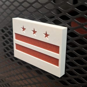 May include: White 3D printed sign with the flag of Washington, D.C. The flag has three white stars on a white background and two red horizontal stripes.