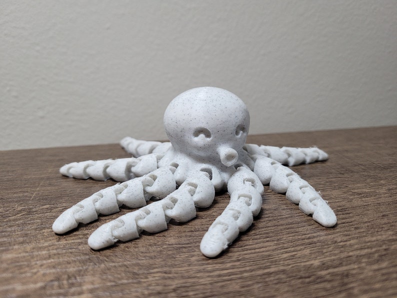 Pu&ograve; includere: Un polpo bianco stampato in 3D con una superficie testurizzata e otto tentacoli segmentati.