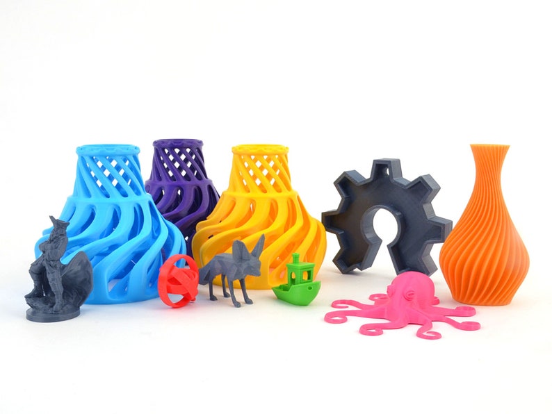 Pu&ograve; includere: Una collezione di oggetti stampati in 3D di vari colori, tra cui un vaso blu, un vaso giallo, un vaso viola, un ingranaggio grigio, un vaso arancione, un polpo rosa, una statuetta grigia, una sfera rossa, una statuetta di animale grigia e una barca verde.