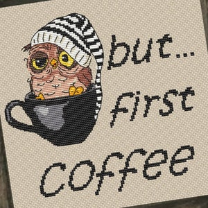 May include: Cross-stitch art piece featuring an owl in a black coffee cup, wearing a striped hat. The text reads "but... first coffee" in black. The artwork is set in a dark wooden frame, perfect for home decor.