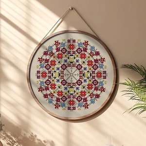 May include: A round wall hanging with a colorful geometric pattern in shades of red, blue, yellow, and white. The pattern is framed in a natural wood frame and hangs from a string.