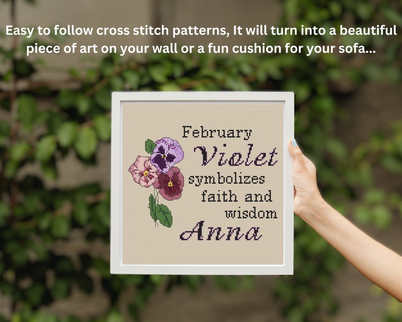 K&ouml;nnte beinhalten: Ein gerahmtes Kreuzstichmuster mit einem floralen Design und dem Text "Februar Veilchen symbolisiert Glauben und Weisheit Anna".