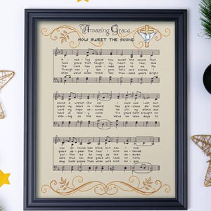 May include: Framed artwork featuring the hymn "Amazing Grace" with musical notes and lyrics. The text is in a decorative font, with a cross and dove symbol. The frame is black, and the background is a light beige color.