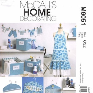 Può includere: Modello di cucito McCall's Home Decorating M6051. L'immagine mostra vari articoli per la casa, tra cui un grembiule, scatole portaoggetti, grucce e un organizer da appendere. Gli articoli presentano motivi floreali e a quadri blu. Il testo "McCall's Home Decorating" è in alto.