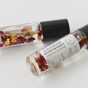 Pode incluir: Dois frascos de &oacute;leo essencial de vidro transparente com tampas pretas. Um frasco est&aacute; aberto, o outro est&aacute; fechado. Os frascos cont&ecirc;m um l&iacute;quido transparente com p&eacute;talas de flores secas e flocos de ouro. O r&oacute;tulo diz "Lavender Peppermint Essential Oil Blend."