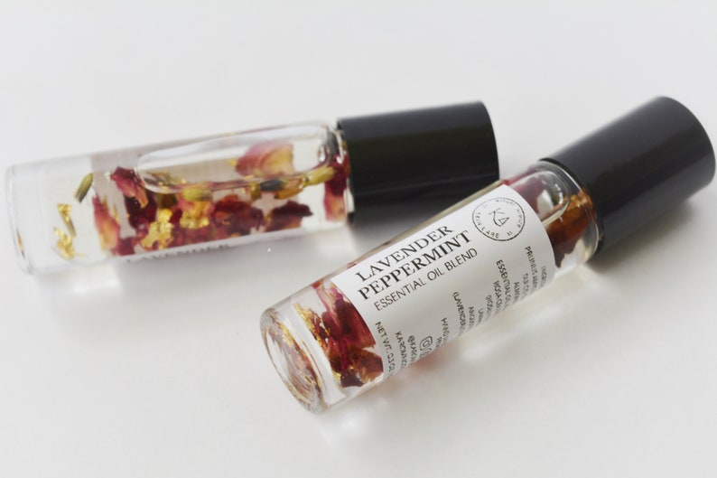 Pode incluir: Dois frascos de &oacute;leo essencial de vidro transparente com tampas pretas. Um frasco est&aacute; aberto, o outro est&aacute; fechado. Os frascos cont&ecirc;m um l&iacute;quido transparente com p&eacute;talas de flores secas e flocos de ouro. O r&oacute;tulo diz "Lavender Peppermint Essential Oil Blend."