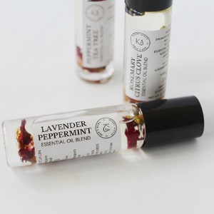 Pode incluir: Frascos de rolo de &oacute;leo essencial de vidro transparente com tampas pretas. Um frasco &eacute; rotulado como "Lavender Peppermint Essential Oil Blend" e cont&eacute;m flores secas. Outros frascos s&atilde;o rotulados como "Peppermint Tea Tree" e "Rosemary Citrus Clove".