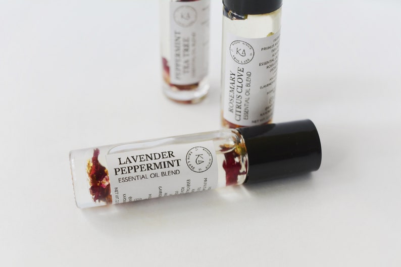 Pode incluir: Frascos de rolo de &oacute;leo essencial de vidro transparente com tampas pretas. Um frasco &eacute; rotulado como "Lavender Peppermint Essential Oil Blend" e cont&eacute;m flores secas. Outros frascos s&atilde;o rotulados como "Peppermint Tea Tree" e "Rosemary Citrus Clove".