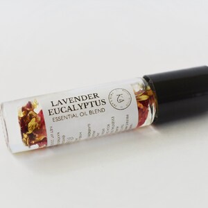 Pode incluir: Frasco roll-on de mistura de &oacute;leos essenciais de vidro transparente com tampa preta. Cont&eacute;m flores secas e flocos de ouro. O r&oacute;tulo diz "Lavender Eucalyptus Essential Oil Blend."