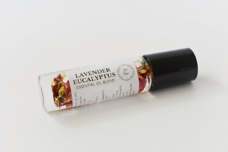 Pode incluir: Frasco roll-on de mistura de &oacute;leos essenciais de vidro transparente com tampa preta. Cont&eacute;m flores secas e flocos de ouro. O r&oacute;tulo diz "Lavender Eucalyptus Essential Oil Blend."