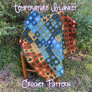Op de afbeelding: Een kleurrijke, handgemaakte gehaakte deken met de woorden "temperature blanket" en "Crochet Pattern" in witte letters. De deken heeft vierkanten in blauw, groen, oranje en geel. Hij is buiten over een kleine houten kruk gedrapeerd.
