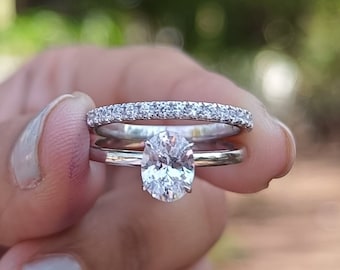 May include: A close-up of a silver oval engagement ring with a diamond center stone. The ring is paired with a matching silver band with small diamonds set in a pave setting.