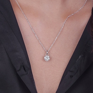 Puede incluir: Un collar de cadena de plata con un pequeño colgante redondo de piedra preciosa transparente.