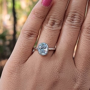 May include: A silver ring with a clear, oval-shaped gemstone. The ring is on a person's finger.