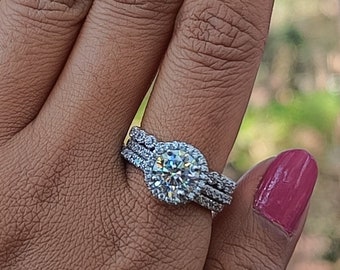 Könnte beinhalten: Nahaufnahme einer Hand, die einen silbernen Ring mit einem großen, runden, klaren Stein trägt, der von kleineren Steinen umgeben ist. Der Ring sitzt auf einem Band mit drei Reihen kleinerer Steine.
