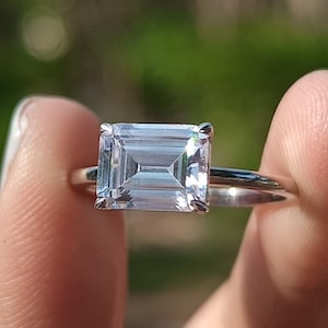 May include: A silver ring with a large, clear, emerald-cut gemstone.