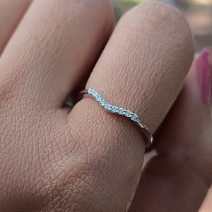 Könnte beinhalten: Ein zarter, gebogener Ring mit einer Reihe kleiner, klarer Steine, die in eine silberne Fassung gefasst sind.