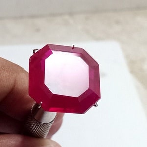 Pode incluir: Uma gema vermelha profunda com um corte octogonal, mantida em uma configuração de metal.