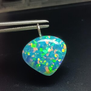 May include: A teardrop-shaped pendant featuring a vibrant blue base with iridescent flecks of neon green, orange, and yellow. The polished stone has a smooth, rounded surface and is attached to a small silver-toned metal bail at the top.