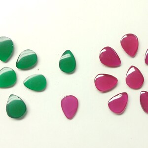 Puede incluir: Una colección de cabujones de piedras preciosas verdes y rosas en forma de lágrima. Las piedras preciosas están dispuestas en un patrón circular.