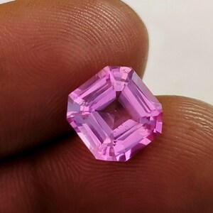 Puede incluir: Una piedra preciosa rosa en forma de octógono con un corte cuadrado. La piedra preciosa está facetada y tiene un alto pulido.