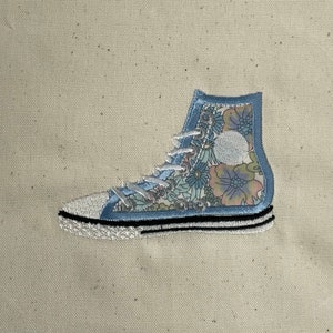 May include: A blue and white floral patterned high-top sneaker with black stitching.