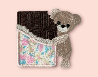May include: Embroidered iron-on patch featuring a brown chocolate bar with a floral pattern and a beige teddy bear hugging the chocolate.