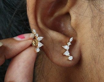 May include: A pair of gold ear climbers with clear cubic zirconia stones. The ear climbers are designed in a geometric shape with a pointed tip.