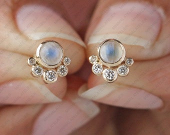 May include: A pair of gold earrings with a moonstone and small diamonds. The moonstone is a milky white color and the diamonds are clear. The earrings are a delicate and feminine design.