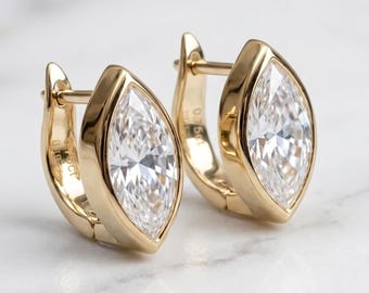 May include: A pair of gold hoop earrings featuring marquise-cut clear stones set in a bezel frame. The earrings have a hinged closure mechanism and are crafted from polished yellow gold, showcasing a sleek design with a faceted center stone.