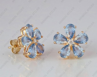 May include: A pair of gold flower-shaped earrings with light blue gemstones. The earrings have a small clear gemstone in the center of each flower.